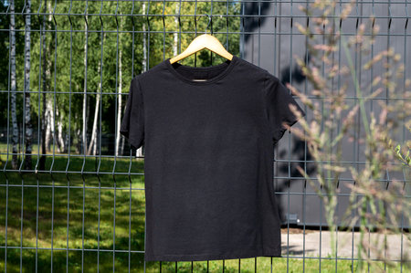 A mockup of a black T-shirt with short sleeves is hanging on a hanger on the streetの写真素材