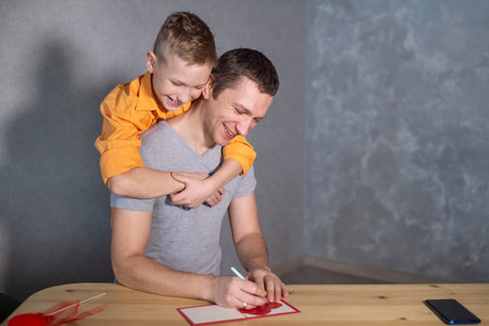 A happy boy hugs his dad. Sign a Valentine's Day card with a heart for a giftの写真素材