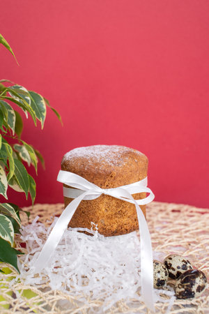 Sponge Easter cake with a white ribbon with quail eggs on a red background with a green plant.の写真素材