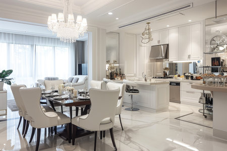 A lavish white kitchen and dining area with chandelier lighting and a well-set tableの素材