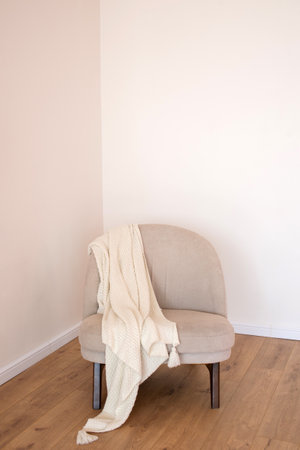 A minimalist interior with a neutral-toned armchair draped with a cream knitted throw on a wooden floor, conveying warmth and simplicityの写真素材
