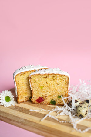 Sliced fruit cake with icing on top, decorated with candied fruits on a wooden board. Studio food...