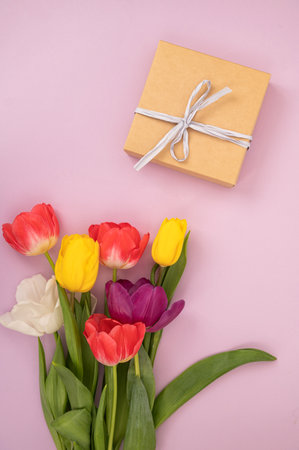 Colorful tulips bouquet and brown gift box on pink background. Mother's Day and birthday concept. Flat lay composition with copy space for design for greeting card, invitation, postcardの写真素材