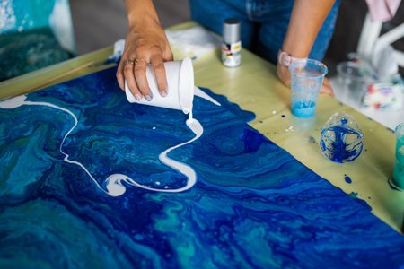Artist's hands pouring white paint on blue swirl acrylic pour artの写真素材