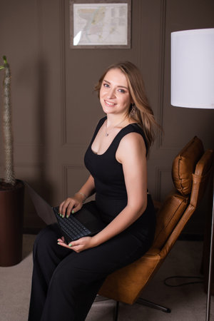 Young woman in business attire working on a laptop with a smileの写真素材