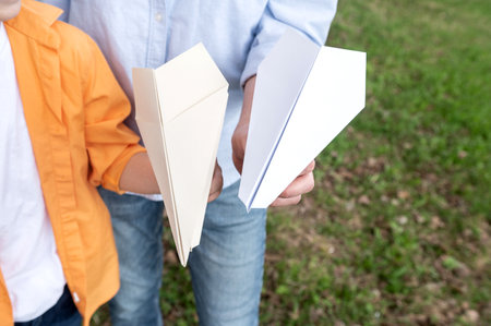 Paper planes in the hands of a man and a child. father's day outdoors in the parkの写真素材