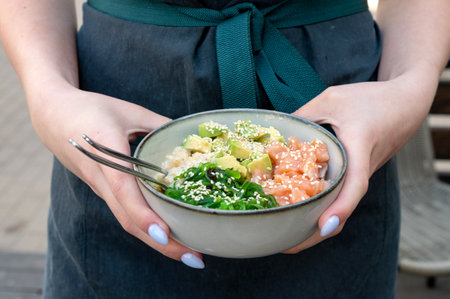 A woman holds a traditional Hawaiian bowling poker in her hands. Hawaiian and Japanese cuisine. Healthy food. poke bowl with seaweed, avocado, cucumber, salmon, sesameの写真素材
