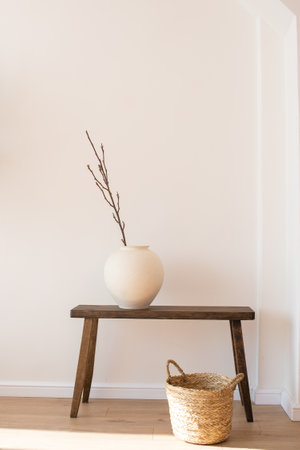 A wooden bench with a rustic aesthetic, a ceramic vase with bare branches, and an indoor olive tree, composing a tranquil cornerの写真素材