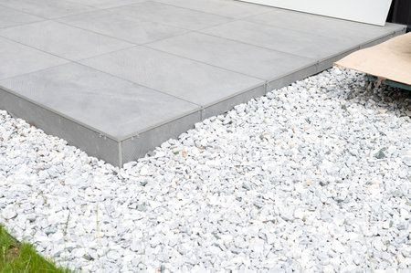 Architectural detail of a modern ramp with gray tiles leading to a building, surrounded by white gravelの写真素材