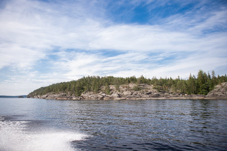 Rocky and stone river bank with fir trees on a sunny day. Water splashes from the boatの写真素材