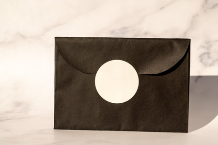 Black envelope with white circular label on marble background. Elegant invitation mockup with copy space for design and brandingの写真素材