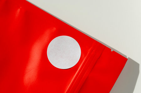 White circular sticker on red poly mailer envelope with natural shadow. Packaging and shipping concept for e-commerce and online retailの写真素材