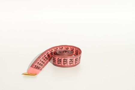 Rolled pink measuring tape on white background with copy space. Diet and tailor concept ideal for design of banner, flyer, and creative projectsの写真素材
