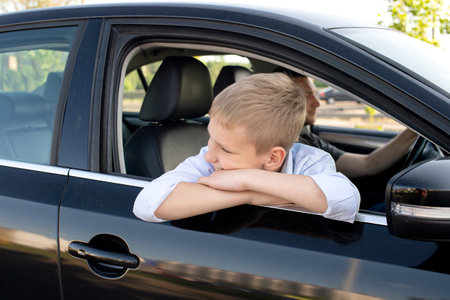 The cute boy climbed out of the car window and looks away. Go with Dad in the car and laugh. Open car windowの写真素材