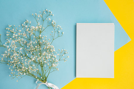 Mockup of a white notebook on a colored blue and yellow background with a bouquet of gypsophila flowersの写真素材