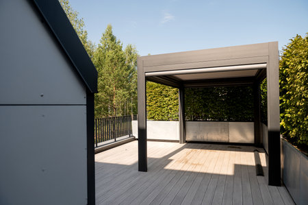 A sleek pergola on a wooden deck, surrounded by trees and clear skiesの写真素材
