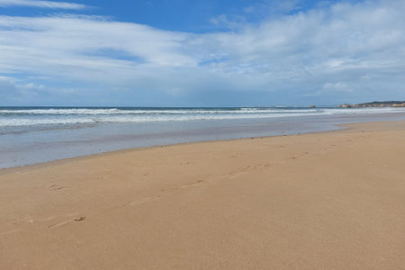 Deserted sandy beach with waves and cloudy sky. Tranquil seascape photography. Travel and relaxation concept. Design for travel poster, wallpaper, backgroundの写真素材