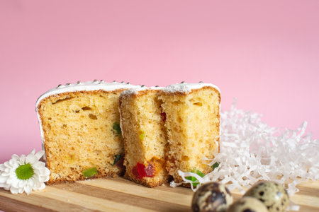 Sliced fruit cake with icing on top, decorated with candied fruits on a wooden board. Studio food photography with pink background and copy spaceの写真素材