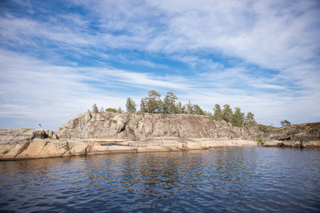 Rocky rocks in the lake on the background of a blue sky with clouds. Stone island with treesの写真素材