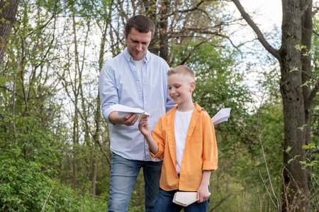 Dad walks with his son with a paper airplane outdoors in the park. Dad and son in shirts holding paper planesの写真素材