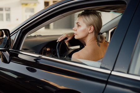Pensive blonde woman with a tattoo driving a car, hand on the steering wheelの写真素材