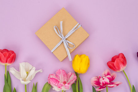 A vibrant arrangement of multicolored tulips surrounding a rustic gift box, all set against a lush purple backdropの写真素材