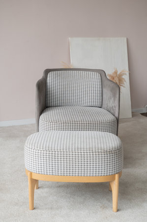 A stylish gray patterned armchair paired with a matching ottoman set against a minimalist decor with artwork in the backgroundの写真素材