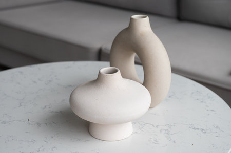 Two elegant, contemporary ceramic vases in neutral tones displayed on a white marble tabletop, embodying minimalist decor aestheticsの写真素材