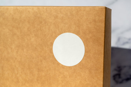 Brown cardboard box with circular white sticker on a neutral background. Simple packaging and branding concept with copy space for design and text placementの写真素材
