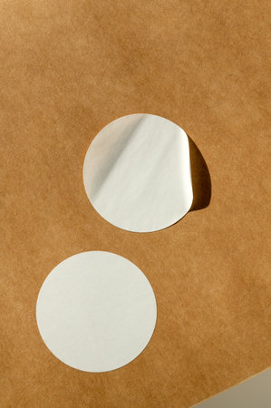 Round white stickers on brown paper background with natural sunlight. Packaging and branding concept for template, mockup designの写真素材