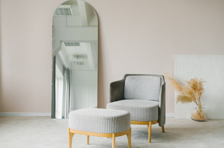 An elegant modern chair paired with a matching ottoman sets a minimalist scene, complemented by a large mirror in a serene interior spaceの写真素材