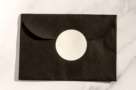 Black envelope with white circular label on marble background. Elegant invitation mockup with copy space for design and brandingの写真素材