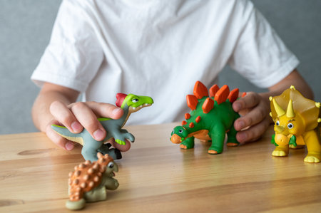 Close-up of a child's hands engaging with colorful toy dinosaurs, showcasing imaginative play on a wooden surfaceの写真素材