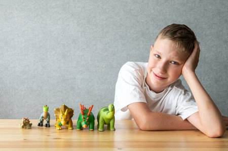A cheerful young boy in a white T-shirt poses alongside his colorful toy dinosaur figures, displaying a mix of happiness and playfulnessの写真素材