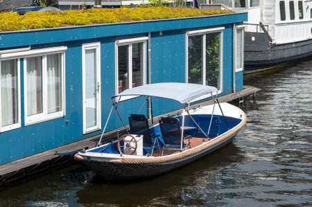 Small motorboat moored next to a blue floating house on a canal.の写真素材