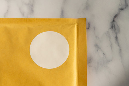 Yellow envelope with white circular sticker on a marble background. Top view envelope packaging mockupの写真素材