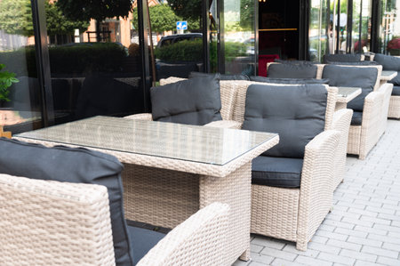 Outdoor cafe seating with wicker furniture and glass table in front of large windows. Street view of a cozy restaurant patioの写真素材