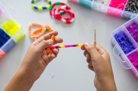 Child making colorful rubber band bracelet with a loom tool.の写真素材