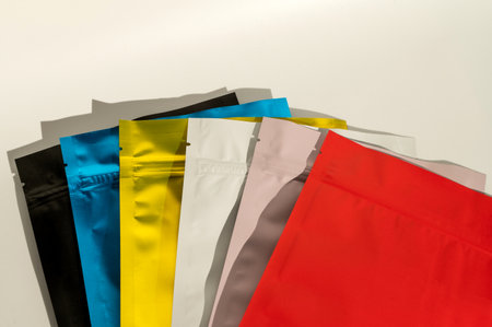 Assortment of colorful packaging pouches arranged in a row on a light background. Top view product packaging mockupの写真素材