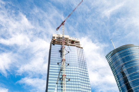 Skyscraper under construction with a crane on a blue sky background. Urban development and architecture conceptの写真素材
