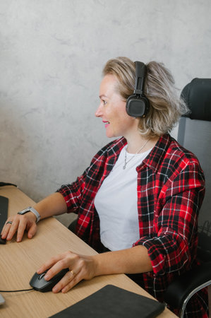 A focused mature woman enjoys music while working on her computer in a casual home office setup