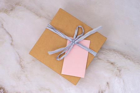 A beautifully wrapped gift box with a blank pink tag tied with a ribbon, set against a luxurious marble backdropの写真素材