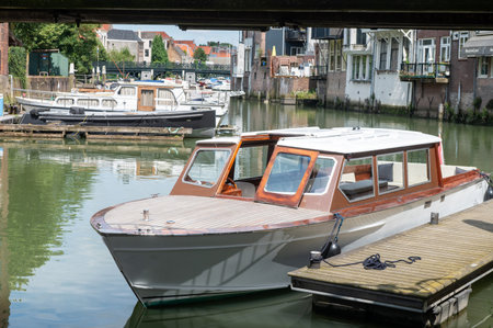 Small wooden boat docked in a peaceful canal surrounded by historic buildings. Nautical and waterfront sceneの写真素材