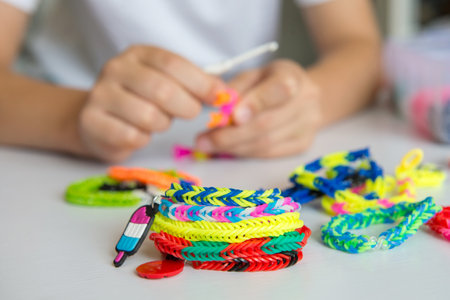 Person making loom bracelets with colorful rubber bands on a white table. Crafting activity in close-up viewの写真素材