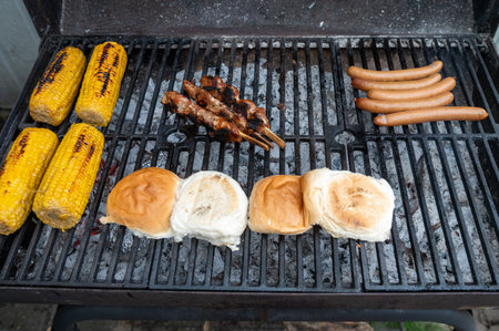Grilled corn, buns, skewers, and sausages on a barbecue grill. Outdoor summer BBQ conceptの写真素材