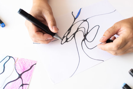 Close-up of hands sketching abstract black lines on white paper with a black marker, emphasizing creativity and artistic expressionの写真素材