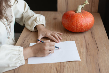 Close-up view of a woman's hands as she delicately sketches a pumpkin, capturing the essence of...