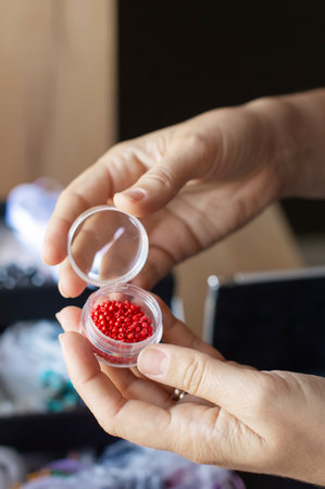 Close-up of a person's hands carefully holding an open container of vibrant red craft beads, showing casing detailed beadworkの写真素材