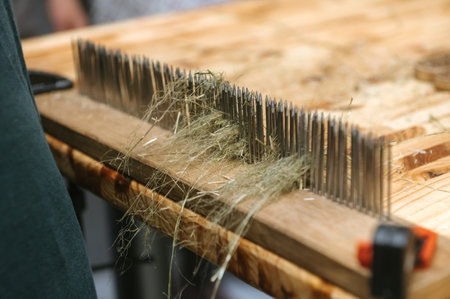 Traditional flax processing with hackling tool on wooden table for craft and textile design.