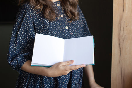 Capture your audience with this image of a woman in a patterned shirt holding an open book with a blank page, ideal for custom messagesの写真素材